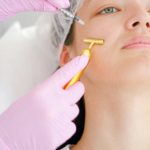 Close-up of a young woman receiving a beauty treatment involving a syringe and face roller at a clinic.