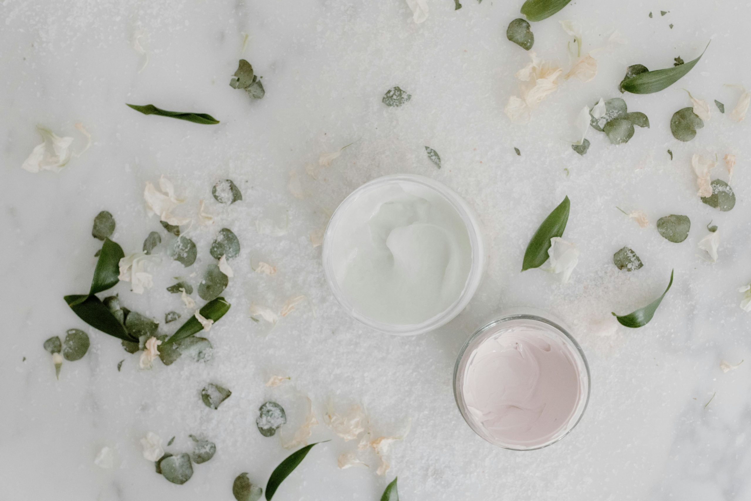 Flat lay of cosmetic cream jars surrounded by natural leaves and petals, perfect for beauty product promotions.